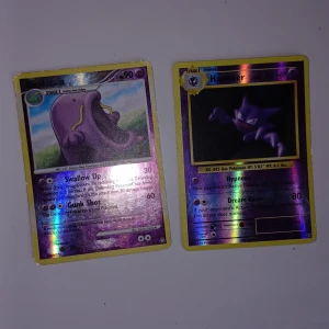 Pokémonkort Swallot och Haunter - Två holografiska Pokémonkort: Swallot och Haunter. Swallot har lila bakgrund och grön ram, Haunter har lila bakgrund och gul ram. Båda korten har klassisk Pokémon-design på baksidan och är på engelska. Båda har lite skråmor på kanterna men inget man märker direkt