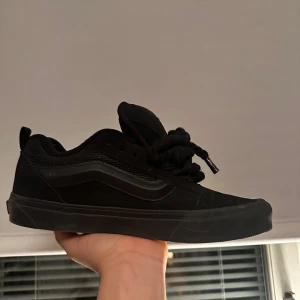 Vans knu skool svart - Klassiska helsvarta Vans sneakers med låg profil och rund tå. Skorna har snörning och är tillverkade i en kombination av canvas och syntetmaterial. Perfekta för en stilren och avslappnad look.