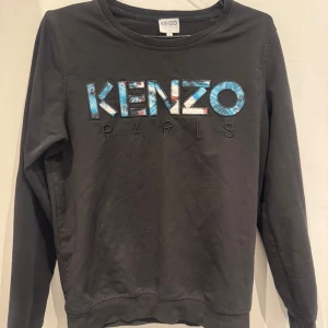 Svart sweatshirt från Kenzo med broderad logga - Svart sweatshirt från Kenzo med broderad logga i blått, vitt och rött framtill. Tröjan har rund halsringning och långa ärmar. Perfekt för en stilren och trendig look.