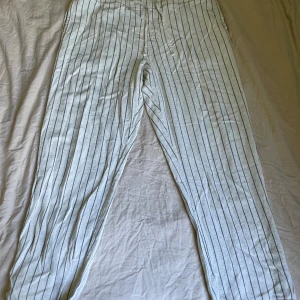 Randiga linnebyxor från H&M - Snygga, ljusa linnebyxor från H&M med svarta vertikala ränder. Byxorna har normal passform och är tillverkade i en skön blandning av viskos och linne. Perfekta för en avslappnad och stilren look.