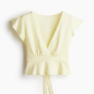 Ljusgul topp med rosett - Superfin ljusgul omlottopp med v-ringning och korta ärmar. Toppen har en knytrosett i midjan och lätt volang nertill. Perfekt för en fräsch och somrig look!