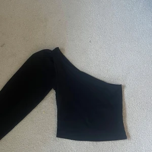 Svart oneshoulder topp - Snygg svart topp med oneshoulder-design och lång ärm. Perfekt för en trendig och stilren look. Supersnygg till sommaren!😍