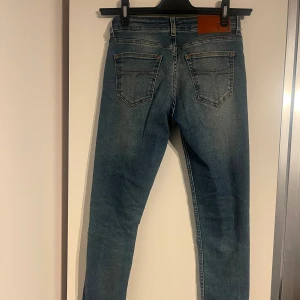 Lågmidjade Jeans Tiger of Sweden - Blåa lågmidjade jeans från tiger of sweden. I bra skick använt fåtal gånger. Hål i knäna storlek W26L30