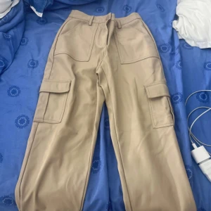 Beiga cargobyxor från Sisters Point - Säljer ett par beiga cargobyxor från Sisters Point med stora fickor på sidorna och normal passform. Byxorna har hög midja, bälteshällor och stängs med knapp och dragkedja. Perfekta för en avslappnad och trendig stil.