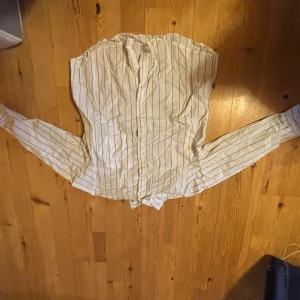 Vit och svart randig skjorta från Divided - Säljer en vit skjorta med svarta ränder från Divided. Skjortan har långa ärmar, klassisk krage och lite oversized, perfekt för en stilren look. Tunn och lätt i materialet, passar bra till många outfits.