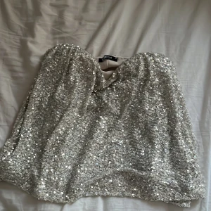 Silver glittrig tubtopp från Gina Tricot - Säljer en superglittrig silver tubtopp från Gina Tricot. Perfekt för att sticka ut med paljetter över hela toppen. Tubmodellen ger en snygg och trendig look. Skriv om ni vill se bilder hur den ser ut på är använd 1 gång aldrig använd annars så är som ny passar Xs och S.