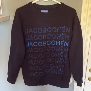Svart sweatshirt från Jacob Cohën - Säljer en svart sweatshirt från Jacob Cohën med tryckt logga i blått framtill. Tröjan har rund halsringning och långa ärmar. Perfekt för en avslappnad och stilren look.