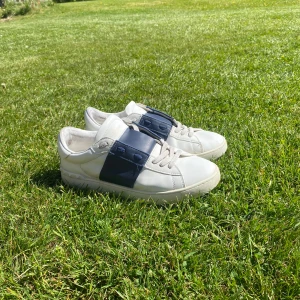 Vita Valentino sneakers med blå detalj - Säljer ett par vita Valentino sneakers med bred blå rem över snörningen. Små hål under skorna. Priset kan diskuteras.