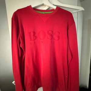 Röd sweatshirt från Hugo Boss - Säljer en röd sweatshirt från Hugo Boss med broderad logga på bröstet. Tröjan har rund halsringning, långa ärmar och är i modern fit. Perfekt för dig som gillar stilrena och klassiska plagg med en touch av färg.