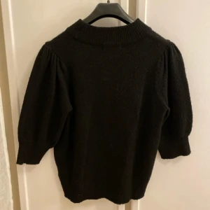 Svart stickad tröja med puffärm - Säljer en svart stickad tröja med  puffiga trekvartsärmar. Tröjan har en klassisk och enkel design med ribbad kant vid halsen. Perfekt att styla till olika outfits. Mycket fint skick.