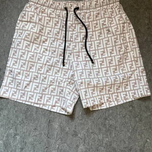 Fendi shorts - Säljer ett par beige och vita badshorts från Fendi med hela shortsen täckta av Fendis klassiska logomönster. Dessa badshorts funkar även för vanlig sommar dag också. Pris kan även diskuteras! Vid fler frågor eller funderingar så är det bara att höra av sig😄