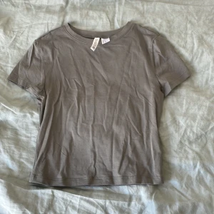 Grön t-shirt från H&M Divided - En basic grön t-shirt från H&M Divided. Modellen har rund halsringning och korta ärmar. Perfekt till jeans eller kjol för en enkel och stilren look. Den är lite kortare och slutar över naveln