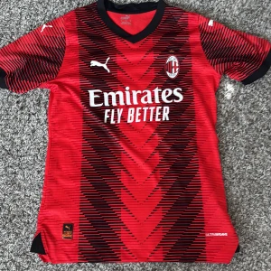AC Milan matchtröja Puma röd/svart - Säljer en AC Milan matchtröja från Puma i rött och svart med svarta detaljer och mönster. Tröjan har korta ärmar, klubbmärke på bröstet och sponsortryck fram och bak. Tillverkad i lätt och ventilerande material.