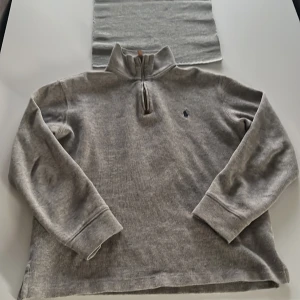 Grå halvzip tröja från Polo Ralph Lauren - Säljer en grå långärmad tröja från Polo Ralph Lauren med halv dragkedja och broderad logga på bröstet. Tröjan har hög krage och är tillverkad i mjukt material, perfekt för lager-på-lager.