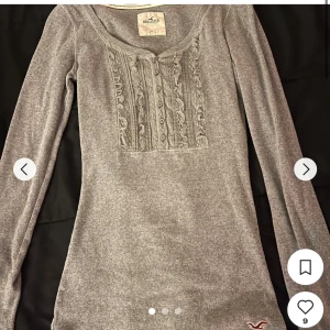 Grå långärmad topp från Hollister - Lånad bild men det är samma tröja! ❤️             Säljer en grå långärmad topp från Hollister med spetsdetaljer och knappar framtill. Tröjan har rund halsringning och är figurnära i modellen. Perfekt till jeans eller kjol. Nypris: 400kr 💝!!