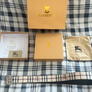  Burberry bälte-Aldrig använt 115cm  - Säljer ett klassiskt Burberry bälte med det ikoniska rutmönstret i beige, svart och vitt. Bältet har ett stilrent silverfärgat spänne med Burberrys logotyp. Perfekt accessoar för att lyfta din outfit.  Hör av dig gärna. Den är oanvänd!