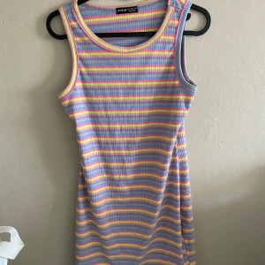 Randig ribbad klänning från Shein - Säljer en ärmlös ribbad klänning från Shein med färgglada ränder i lila, gul, rosa och blå. Klänningen har en rund halsringning och är i en mjuk, stretchig bomullsblandning. Perfekt för varma dagar!