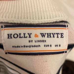 Vit och svart randig stickad tröja från Holly & Whyte - Säljer en vit stickad tröja från Holly & Whyte med svarta horisontella ränder. Tröjan har korta ärmar, rund halsringning och bred ribbad mudd i midjan. Perfekt för en klassisk och stilren look.