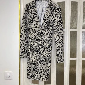 Svartvit mönstrad kappa från H&M - Säljer en svartvit kappa från H&M med ett unikt abstrakt mönster. Kappan har lång ärm, knappar framtill och klassisk krage. Perfekt för dig som vill sticka ut med en trendig och stilren look.