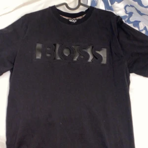 Hugo boss - Svart t-shirt från BOSS med stor, upphöjd BOSS-logga i svart på bröstet. Klassisk rund halsringning och korta ärmar. Perfekt för en stilren och enkel look. Väldigt bekväm att ha på sig:)