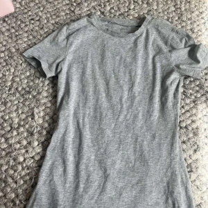 Grå t-shirt från Intimissimi - En enkel och stilren grå tajt t-shirt från Intimissimi i mjuk bomull. Modellen har rund halsringning och korta ärmar, perfekt för en clean och avslappnad look.