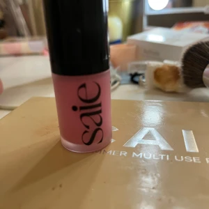 Flytande mini rouge från Saie i rosa nyans - Flytande rouge från Saie i en härlig rosa färg. Kommer i en smidig tub med svart lock och tydlig logga. Perfekt för att ge kinderna en fräsch och naturlig färg. Konsistensen är krämig och lätt att blenda ut. Endast testad