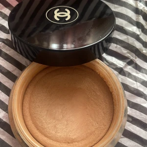 Chanel bronzer i krämform - Lyxig bronzer från Chanel i en stor rund burk med svart lock och ikonisk logga. Krämig formula i en varm, gyllenbrun nyans som ger en naturlig solkysst look. Perfekt för att skulptera och ge lyster till ansiktet. Les beige. 