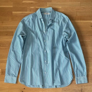Randig skjorta från Burberry - Säljer en klassisk randig skjorta från Burberry London i storlek S. Skjortan har blå, gröna och vita ränder, långa ärmar och knäppning framtill. Perfekt för dig som gillar stilrena och tidlösa plagg.
