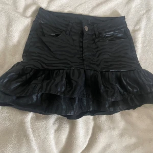 jeanskjol  - Svart jeanskjol med mönster och volang, passar perfekt till sommaren! Har sytt själv, totala midjemått är 66cm!