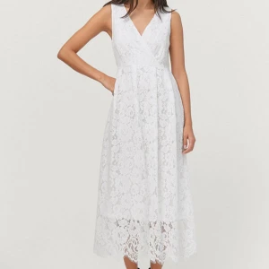 Vit spetsklänning från Ellos - Superfin vit långklänning från Ellos i spets med v-ringning och omlottliv. Klänningen har ärmlös design och vackert blommigt spetsmönster, perfekt för sommarens tillfällen. Fodrad under spetsen för extra komfort.