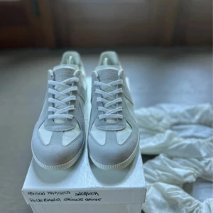 Maison Margiela gats - Maison Margiela sneakers i vitt och ljusgrått skinn och mocka. Snygg minimalistisk design med vita och grå. Perfekta för dig som gillar stilrena och exklusiva sneakers eller bara något nytt inför sommaren. Pris går att diskutera vid smidig affär.