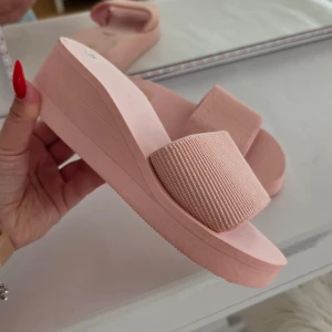 Rosa platåsandaler med bred rem - Säljer ett par snygga rosa sandaler med platåsula och bred ribbad rem över foten. Perfekta för sommaren och ger en trendig look med sin höga sula och stilrena design.