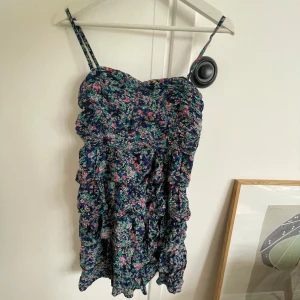 Klänning  - Blommig klänning med volanger. Justerbara och avtagbara band. Stretchig så passar allt från S-XL