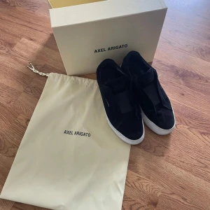 Svarta sneakers från Axel Arigato - Säljer ett par svarta sneakers från Axel Arigato med vit sula och diskret logga på sidan. Skorna är i mocka och har en stilren design utan snörning, köpte dessa skor på Plick men tyckte inte riktigt det var min still så väljer att sälja vidare. Pris kan diskuteras!