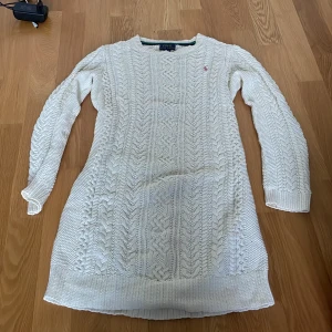 Vit stickad klänning från Polo Ralph Lauren - Vit stickad klänning från Polo Ralph Lauren med klassiskt kabelstickat mönster och lång ärm. Liten broderad logga i rosa på bröstet. Perfekt för en middag eller skolavslutning. Använder tyvärr inte och därför väljer jag att sälja den. Pris kan diskuteras. 