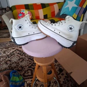 Vita Converse Chuck Taylor All Star sneakers - Säljer ett par vita Converse Chuck Taylor All Star sneakers med högt skaft och kraftig platåsula. Skorna har klassisk snörning och svart rand längs sulan. Perfekta för dig som gillar en sportig och trendig stil.
