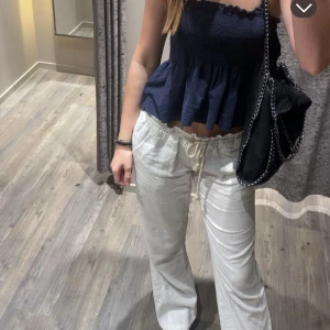 Vita linnebyxor med dragsko - Säljer ett par vita linnebyxor med avslappnad passform och dragsko i midjan. Byxorna har raka ben, resår i midjan och fickor både fram och bak. Perfekta för varma dagar och enkel att styla med olika toppar.