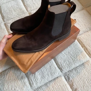 Bruna Chelsea boots från Berwick - Snygga bruna Chelsea boots från Berwick i mjuk mocka. De har en klassisk design med elastiska paneler på sidorna och en dragflik baktill för enkel påtagning. Perfekta för en stilren look. Nypris: 3000kr. Passar 43-44