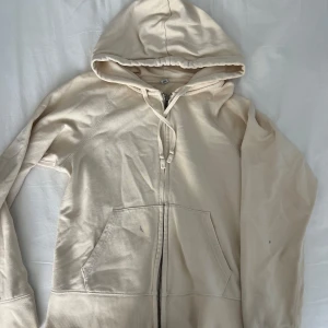 Beige hoodie från Uniqlo - Säljer en beige hoodie från Uniqlo med dragkedja och fickor framtill. Den har en justerbar huva med snören.