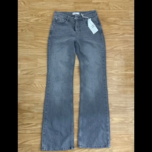 Grå jeans flare - Snygga grå jeans med flare i full längd petite. Perfekta för en stilren look. De har en klassisk design med fem fickor och knappgylf. Passar utmärkt för både vardag och mer uppklädda tillfällen.