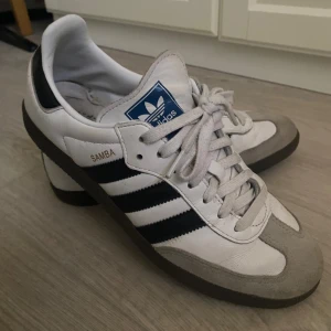 Adidas Samba sneakers - Klassiska Adidas Samba sneakers i vitt och svart med grå detaljer. Köpta från Zalando något år tillbaka för 1 325 kr. Använda men inte söndags på något sätt. De mest bekväma skorna nånsin! Har inte testat att putsa upp dom än.