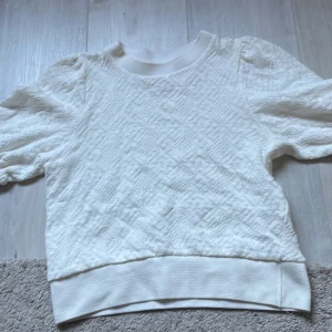 Vit tröja från Holly & Whyte - Säljer en vit tröja från Holly & Whyte by Lindex. Tröjan har ett subtilt mönster och korta ärmar. Perfekt för en stilren look. 👀 