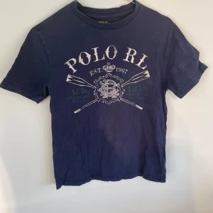 Blå t-shirt från Ralph Lauren - Säljer en blå t-shirt från Ralph Lauren med tryck framtill. T-shirten har korta ärmar och rund halsringning. Perfekt för en avslappnad stil säljer en liknande annons köp gärna ett bundel .