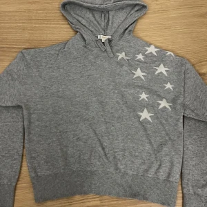 Grå hoodie med stjärnmönster - Säljer en grå hoodie med en cool stjärndesign på framsidan och en stor stjärna på baksidan. Tröjan har en bekväm passform med långa ärmar och en praktisk huva. Perfekt för en avslappnad stil. 