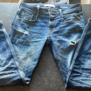 Replay jeans - Snygga blå jeans från Replay, modell Anbass. De har en klassisk femficksdesign med slitna detaljer. Perfekta för en avslappnad stil. Hör av er vid minsta fråga 