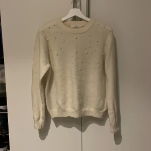 Vit tröja med pärlor - Säljer en stilren creme färgad tröja dekorerad med pärlor på framsidan. Tröjan har långa ärmar och en rund halsringning. Perfekt för att ge en elegant touch till din outfit. Endast använd ett fåtal gånger 