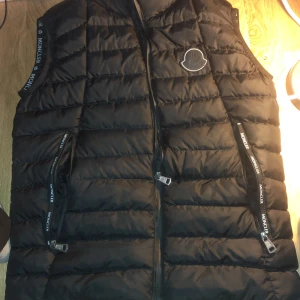 Svart dunväst från Moncler - Snygg svart (äkta) Moncler dunväst med dragkedja och ikonisk logga på bröstet. Västen har en quiltad design och praktiska fickor med dragkedjor. Perfekt för kyligare dagar när du vill hålla stilen. ja säljer den för att jag behöver pengar hur fort somhelst priset kan gå ner om ni vill ej kvitto och box
