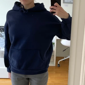 Mörkblå hoodie från H&M Divided - Säljer en mörkblå hoodie från H&M Divided i storlek XXS. Den har en klassisk design med en stor ficka framtill och justerbar huva med dragsko. Perfekt för många tillfällen.