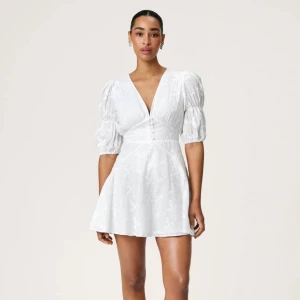 Adorore klänning - vit blommig klänning med puffärmar - Säljer en söt vit klänning från adoore med blommigt mönster och puffiga trekvartsärmar. Klänningen har en v-ringad design och knappar framtill. Perfekt för sommaren och kanske studenten eller skolavslutning! Endast använd 1 gång!