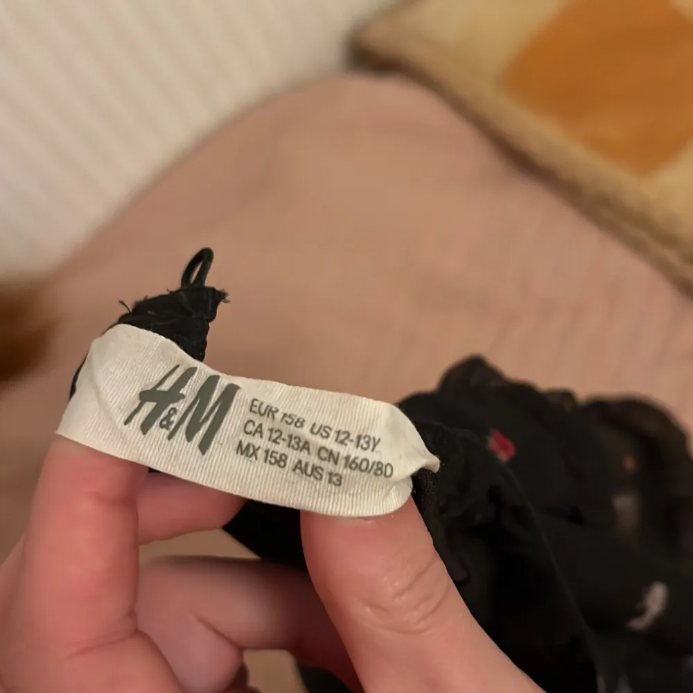 Säljer en söt svart blus från H&M med små blommiga detaljer. Blusen har korta ärmar och en luftig passform, perfekt för både vardag och speciella tillfällen. 🌸. Yläosat.